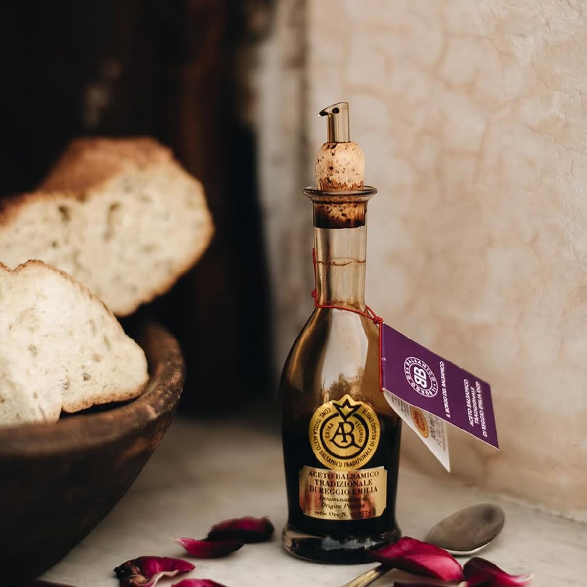 Bottle of olive oil with a cork stopper on a table with bread and petals.
