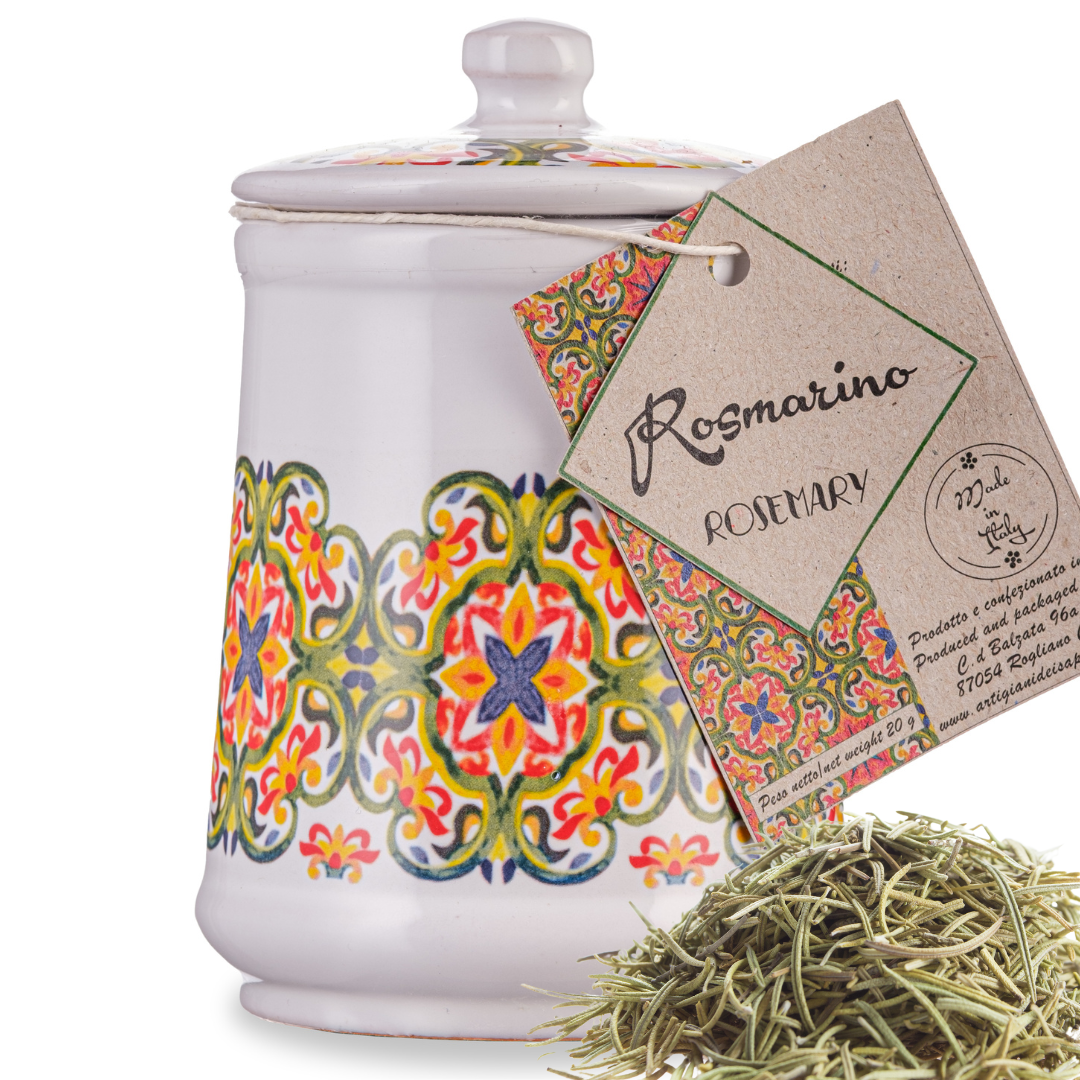 A colorful Italian handmade ceramic jar labeled 'Rosmarino' with a lid, containing dried rosemary spice, alongside a tag and a small pile of dried rosemary leaves.