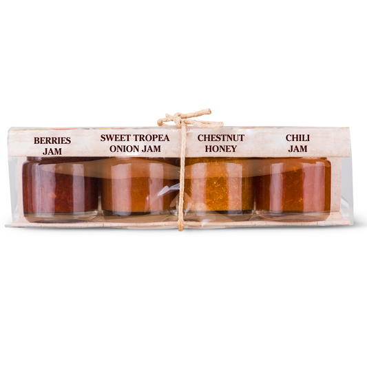 A packaged set of four glass jars containing cheese board condiments with labels indicating the flavors, Sweet Tropea Red Onion Jam, Chili Honey, Chestnut Honey, and Mixed Berries Jam.