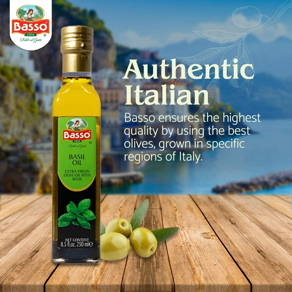 Basso basil oil extra virgin olive oil bottle with olives on wooden table and Italian coastal background.