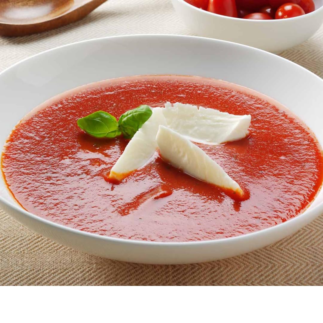 Creamy red tomato soup served in a white bowl, garnished with fresh basil and mozzarella slices.