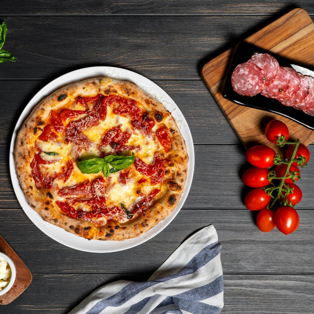 Authentic Italian pizza topped with melted cheese, tomato sauce, and fresh basil, served on a white plate with salami slices, fresh vine tomatoes, and mozzarella on the side