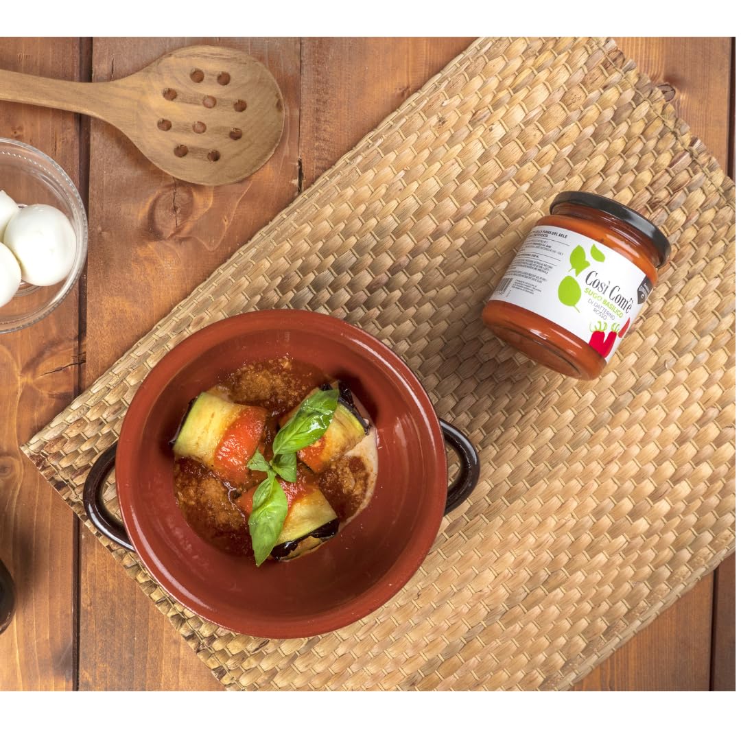 Top view of an Italian dish prepared with Così Com’è Red Datterino Tomato Sauce with Basil, served in a terracotta bowl with fresh basil garnish. A jar of the sauce is placed on a woven mat beside the dish.