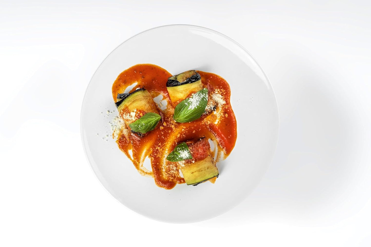 Elegant plate of Italian eggplant rolls topped with tomato sauce, fresh basil leaves, and grated Parmesan cheese, served on a white background.