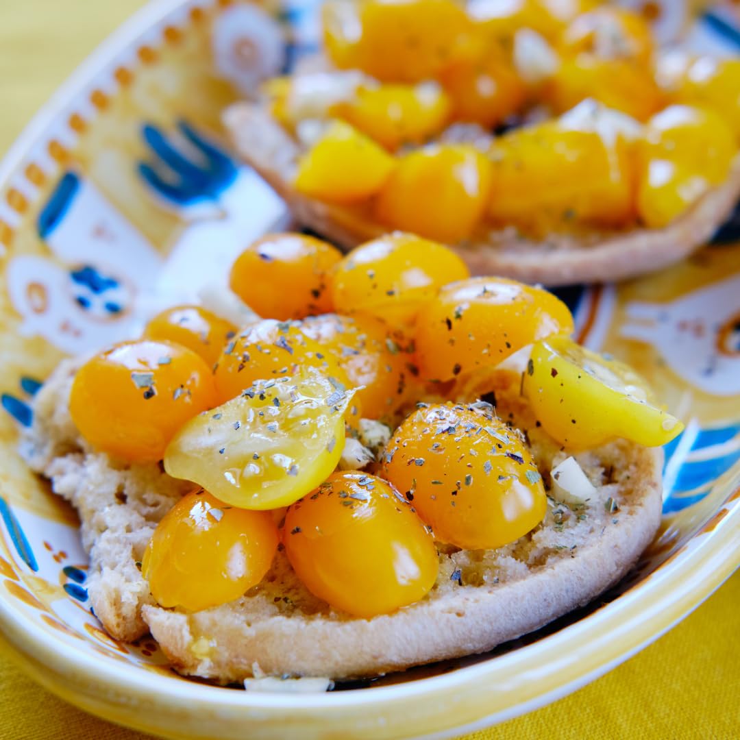 Close-up of toasted bread topped with fresh yellow datterini tomatoes, garlic, olive oil, and herbs, served on a decorative ceramic plate