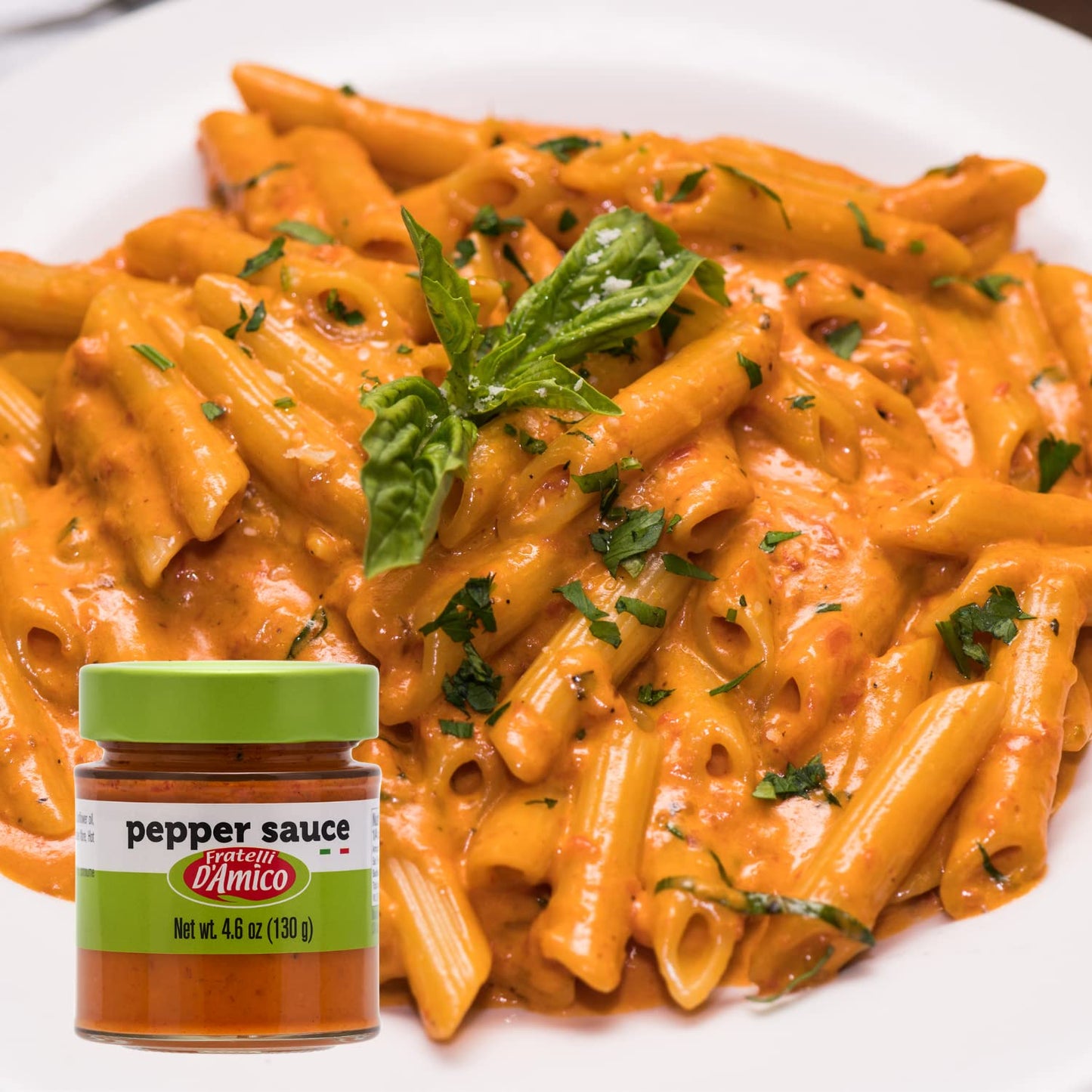 Plate of creamy penne pasta cooked with Fratelli D’Amico Red Pepper Pesto Sauce, garnished with fresh basil and parsley, with the 4.6 oz (130 g) jar of pepper sauce displayed in the foreground.