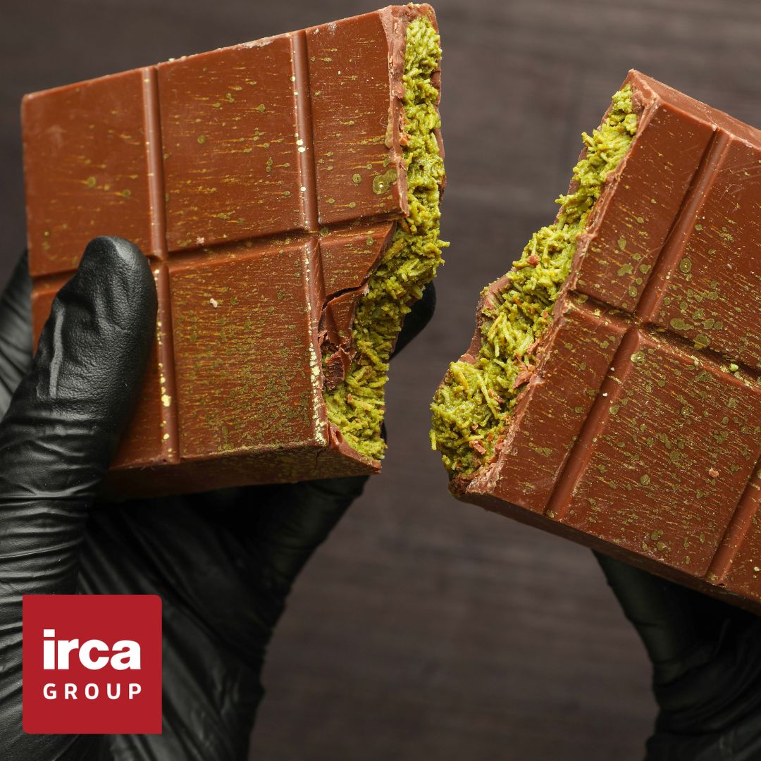 Dubai Chocolate bar with green herb-like substance held by a person wearing black gloves, Irca Group logo visible.