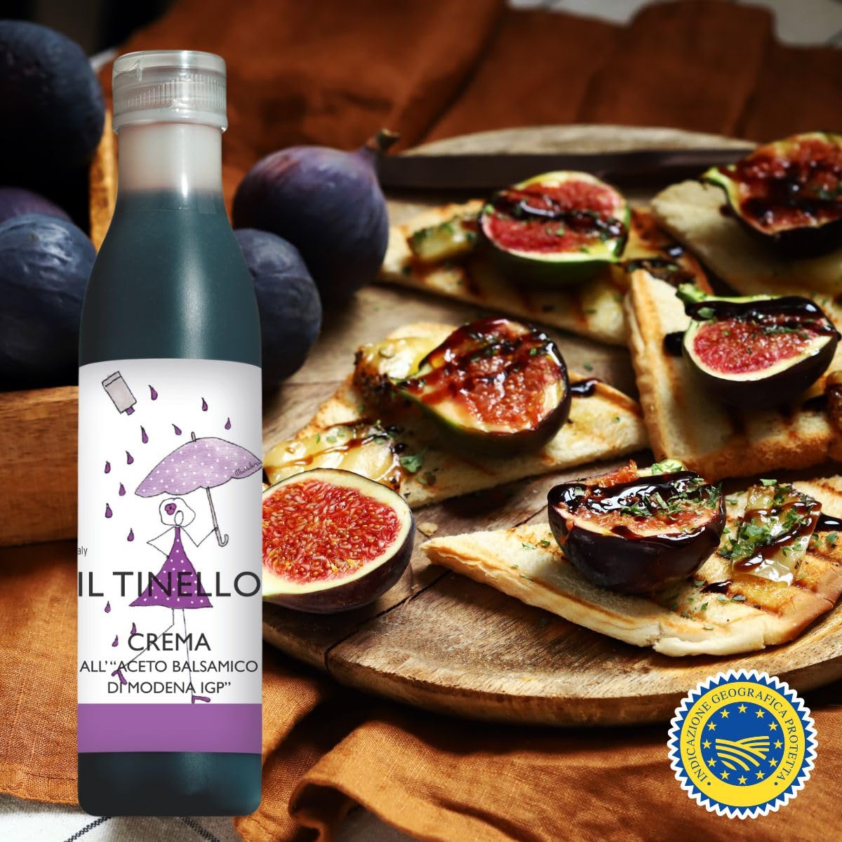 Bottle of Il Tinello Crema with a plate of fig-topped pizzas on a wooden surface.