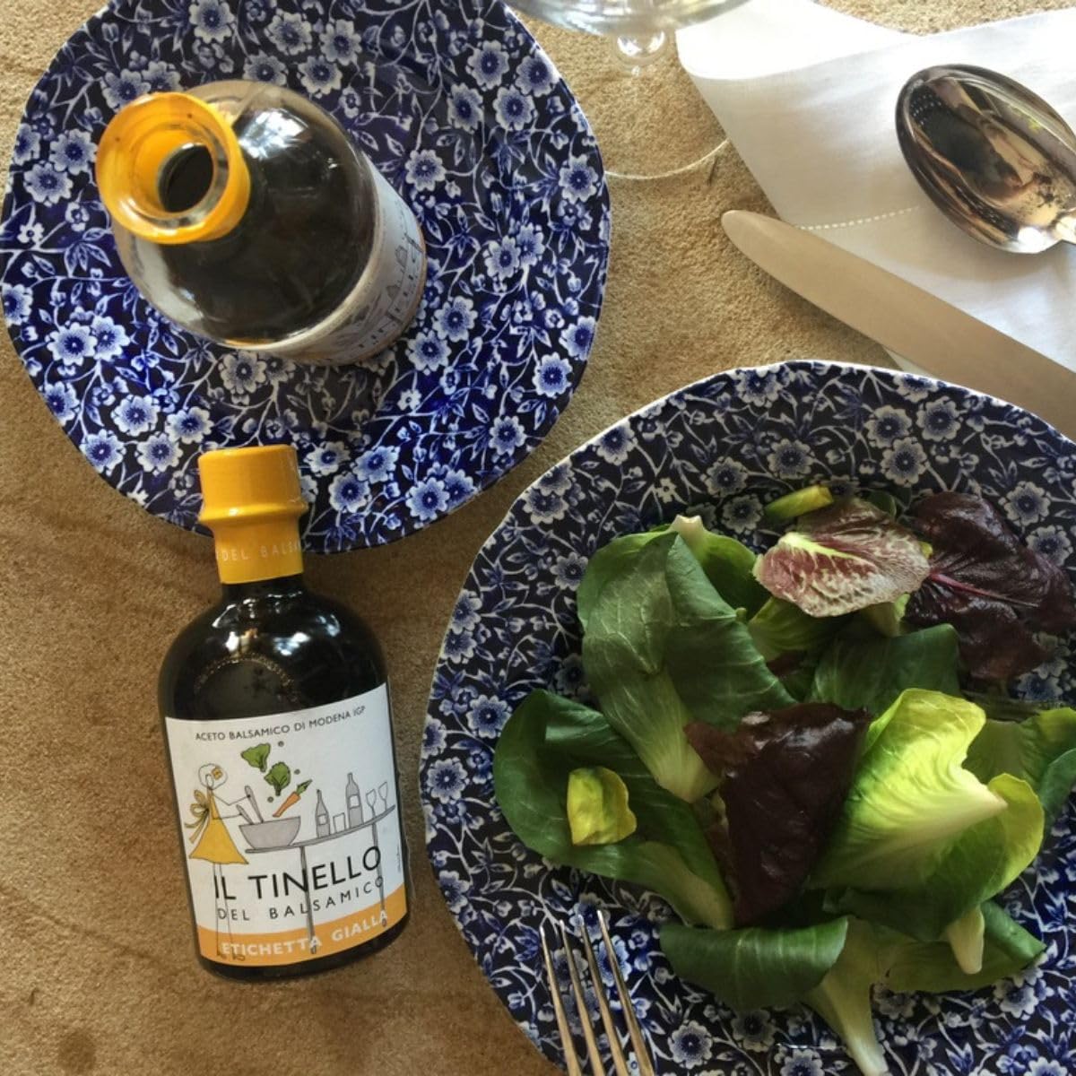 Bottle of Il Tinello balsamic vinegar on a table with a plate of salad.