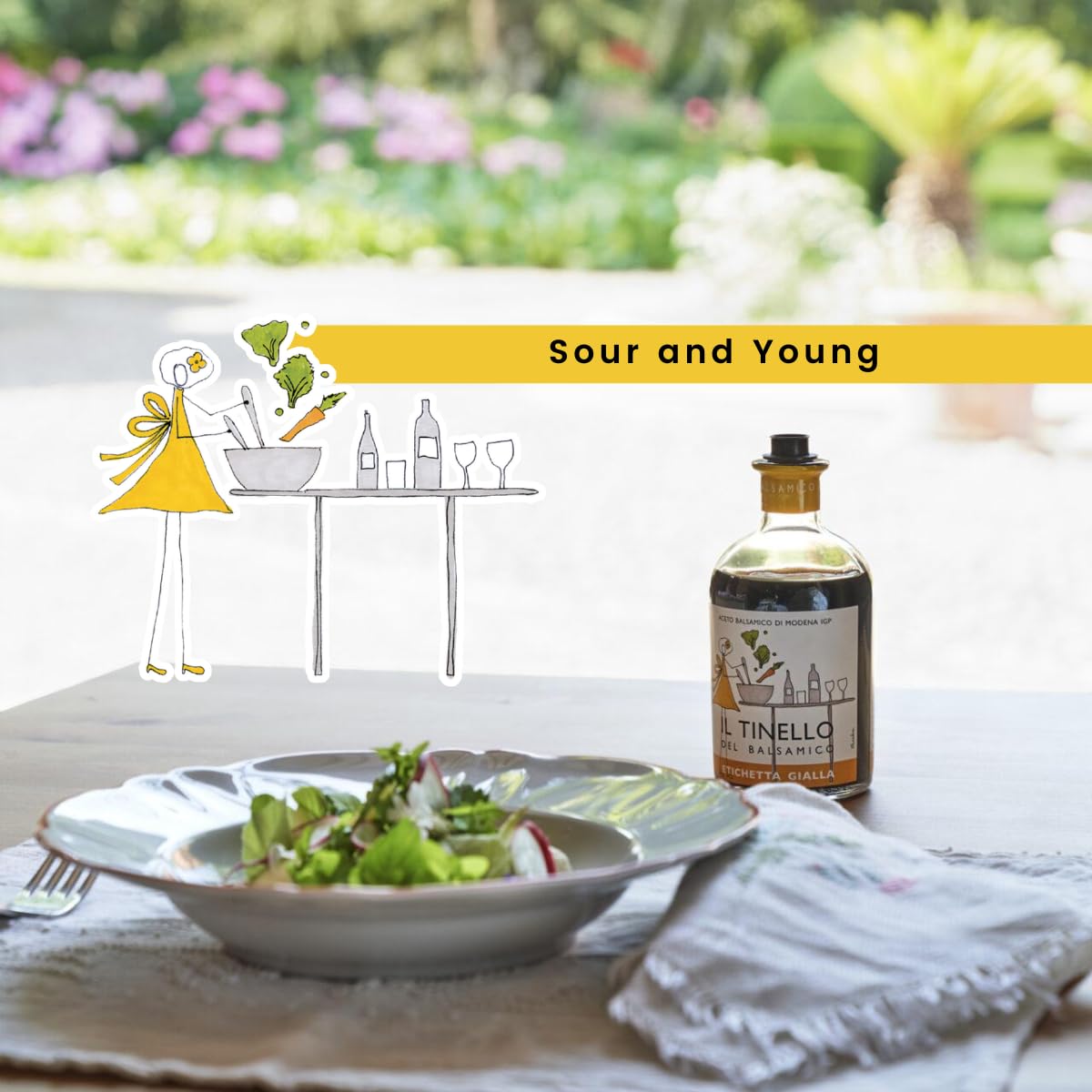 Bottle of TINELLO olive oil with a salad on a table outdoors, featuring 'Sour and Young' branding.