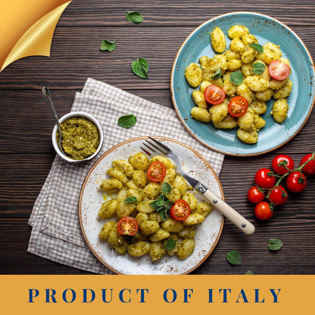 Two plates of potato gnocchi with pesto and cherry tomatoes, served with fresh herbs and sauce on a wooden table.