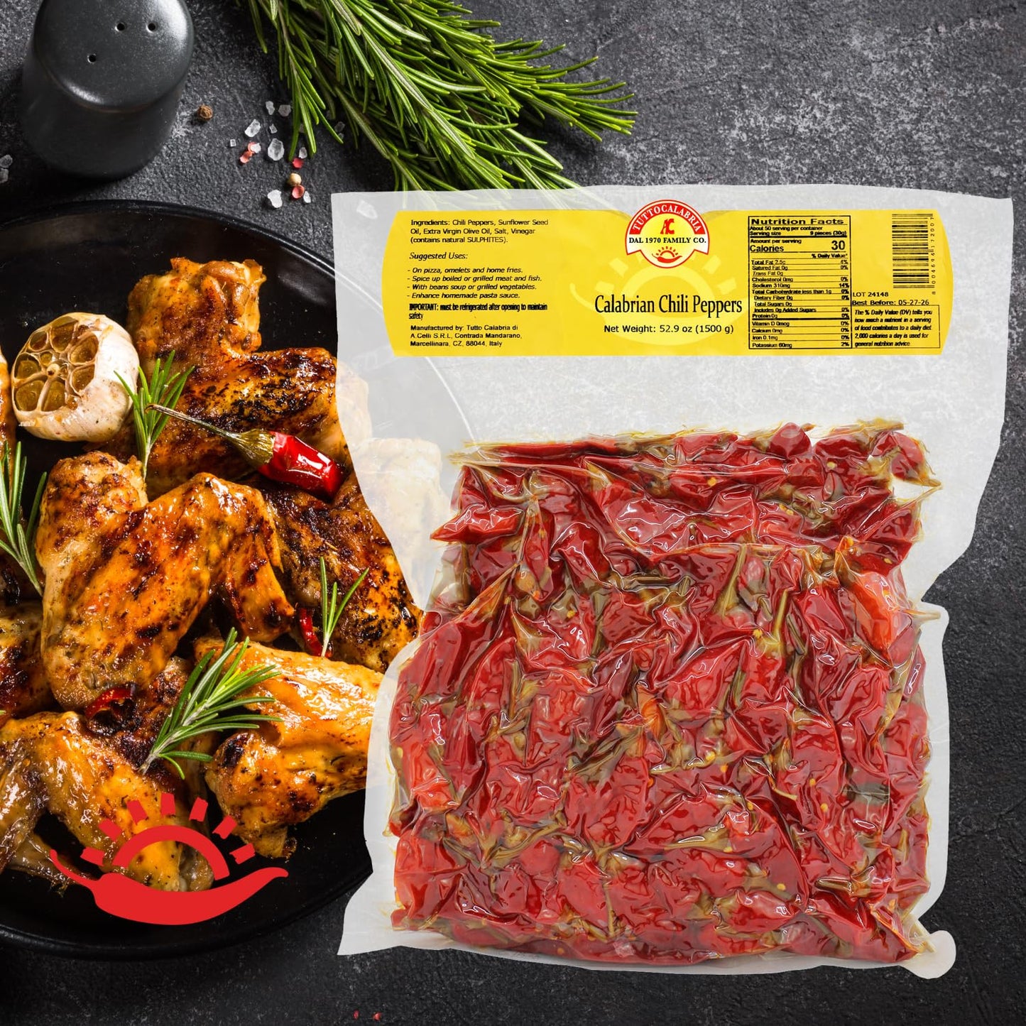 Packaged Calabrian chili peppers with a dish of roasted chicken and herbs on a dark surface.