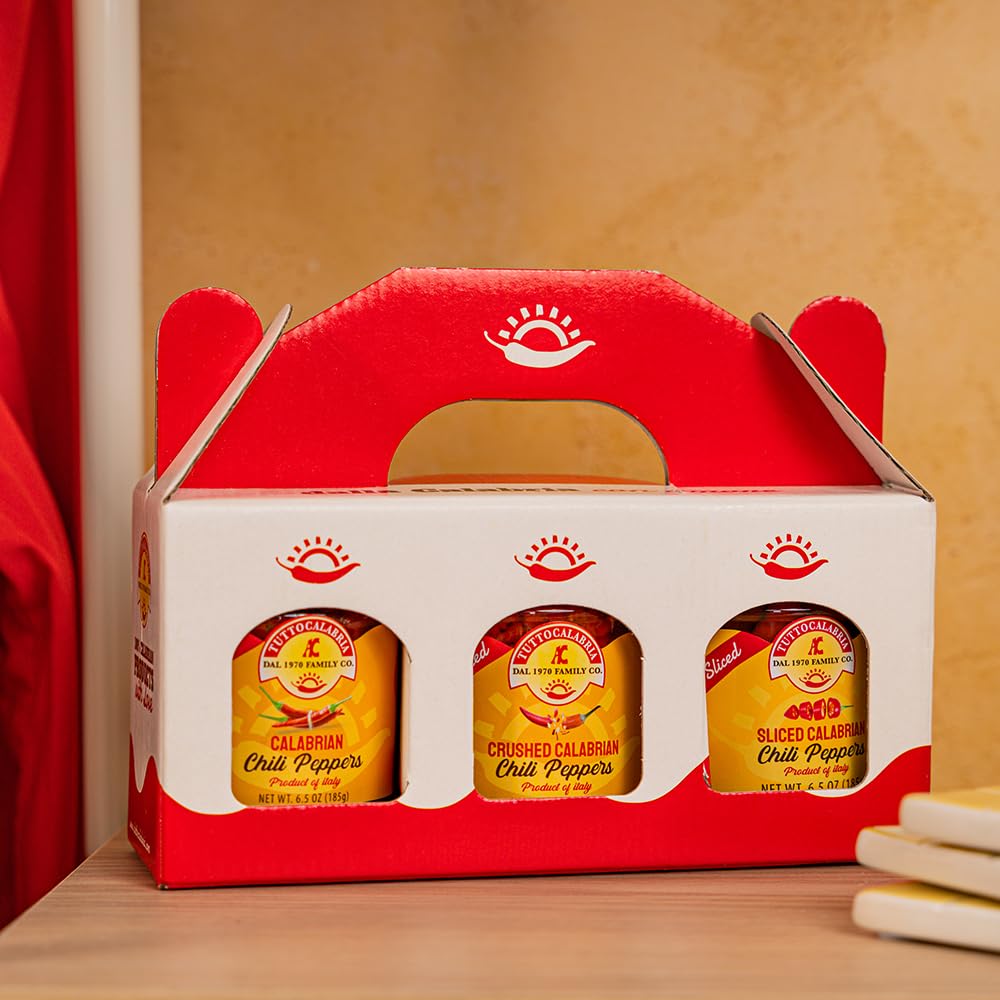 Red and white packaging box with three jars of TuttoCalabria calabrian chili peppers on a wooden surface.