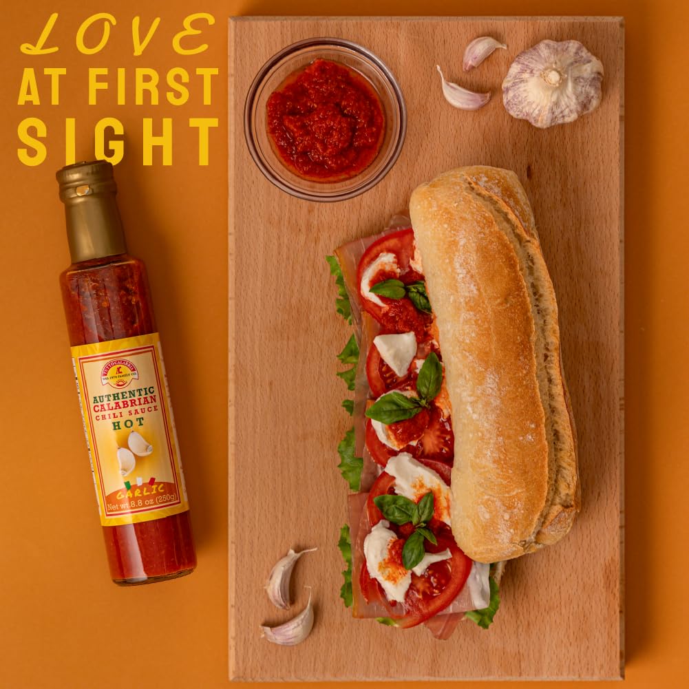 Bottle of TuttoCalabira hot sauce next to a sandwich on a wooden board with text 'Love at First Sight' on an orange background.