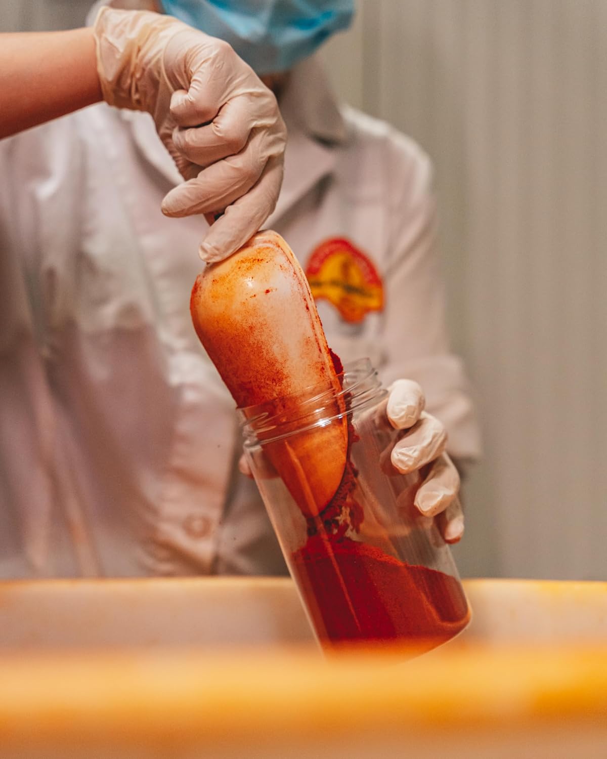 Person in protective gear holding a container with a red liquid and orange object.