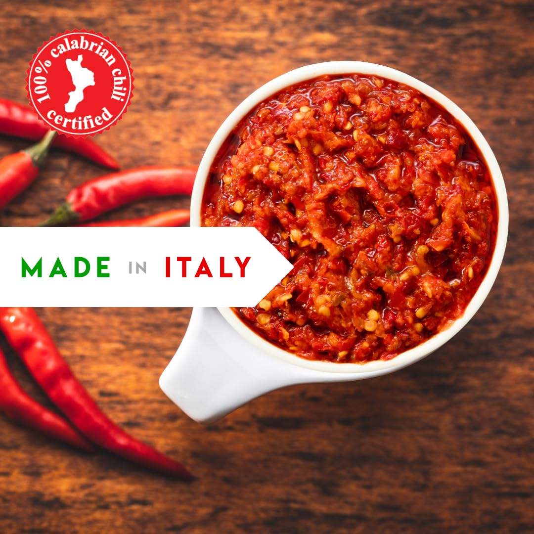 White bowl filled with red chili paste on a wooden surface with red chili peppers, '100% Calabrian Chili Certified' logo, and 'Made in Italy' text.