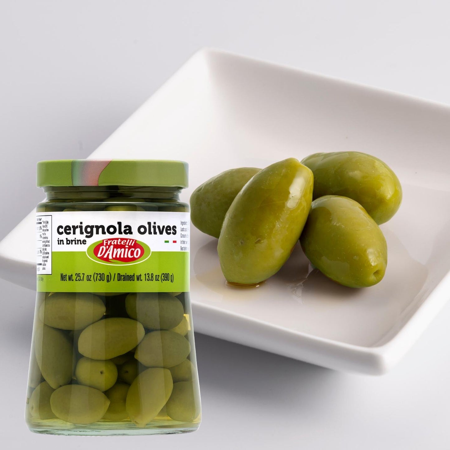 Jar of Fratelli D’Amico Green Cerignola Olives in brine (25.7 oz / 730 g) placed next to a white dish with several large, glossy green olives, highlighting their size and fresh texture.
