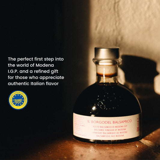 Bottle of Balsamic vinegar with a label and text about Modena I.G.P. on a wooden surface.