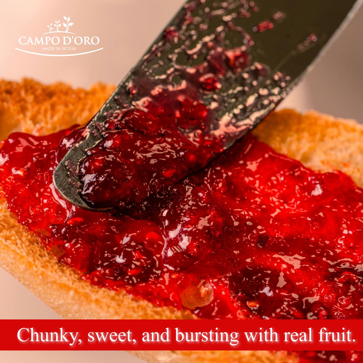 Red jam being spread on bread with a knife, featuring Campo d'Oro logo.