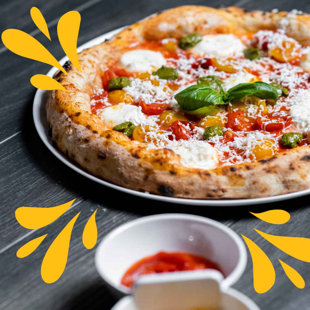 Authentic Italian pizza topped with mozzarella cheese, fresh basil, cherry tomatoes, and pesto, made with Così Com’è Datterini tomato sauce, served on a rustic black wooden table with parmesan and cured meat on the side