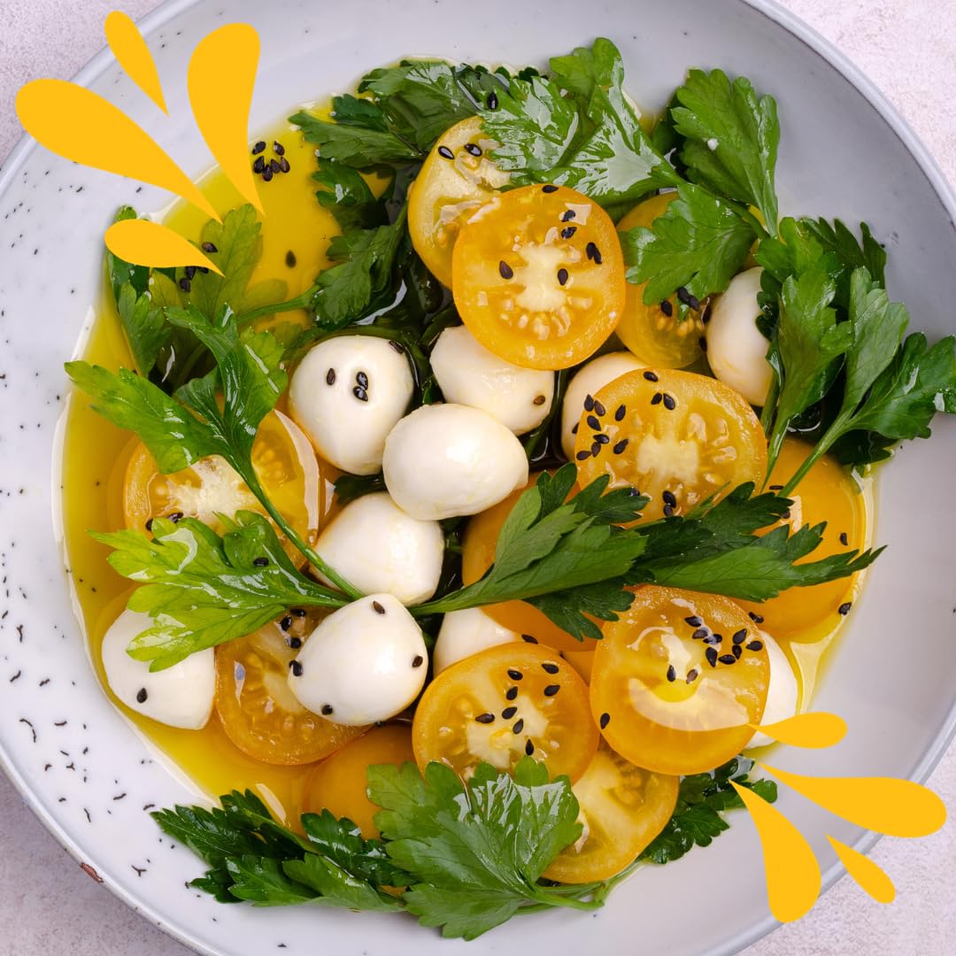 Fresh salad of yellow datterino tomatoes with mozzarella balls, parsley, black sesame seeds, and olive oil, served in a white bowl for a colorful Mediterranean dish.