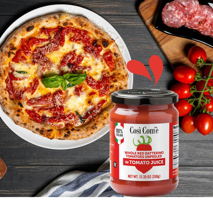 Così Com’è Whole Red Datterino Tomatoes in Tomato Juice jar (12.35 oz / 350 g) displayed next to a freshly baked pizza topped with melted cheese, basil, and red Datterino tomatoes, with fresh vine tomatoes and slices of salami in the background.