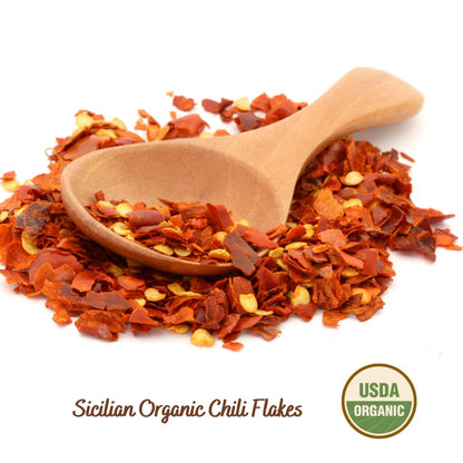Sicilian Organic Chili Flakes with a wooden scoop on a white background, featuring an USDA Organic label.