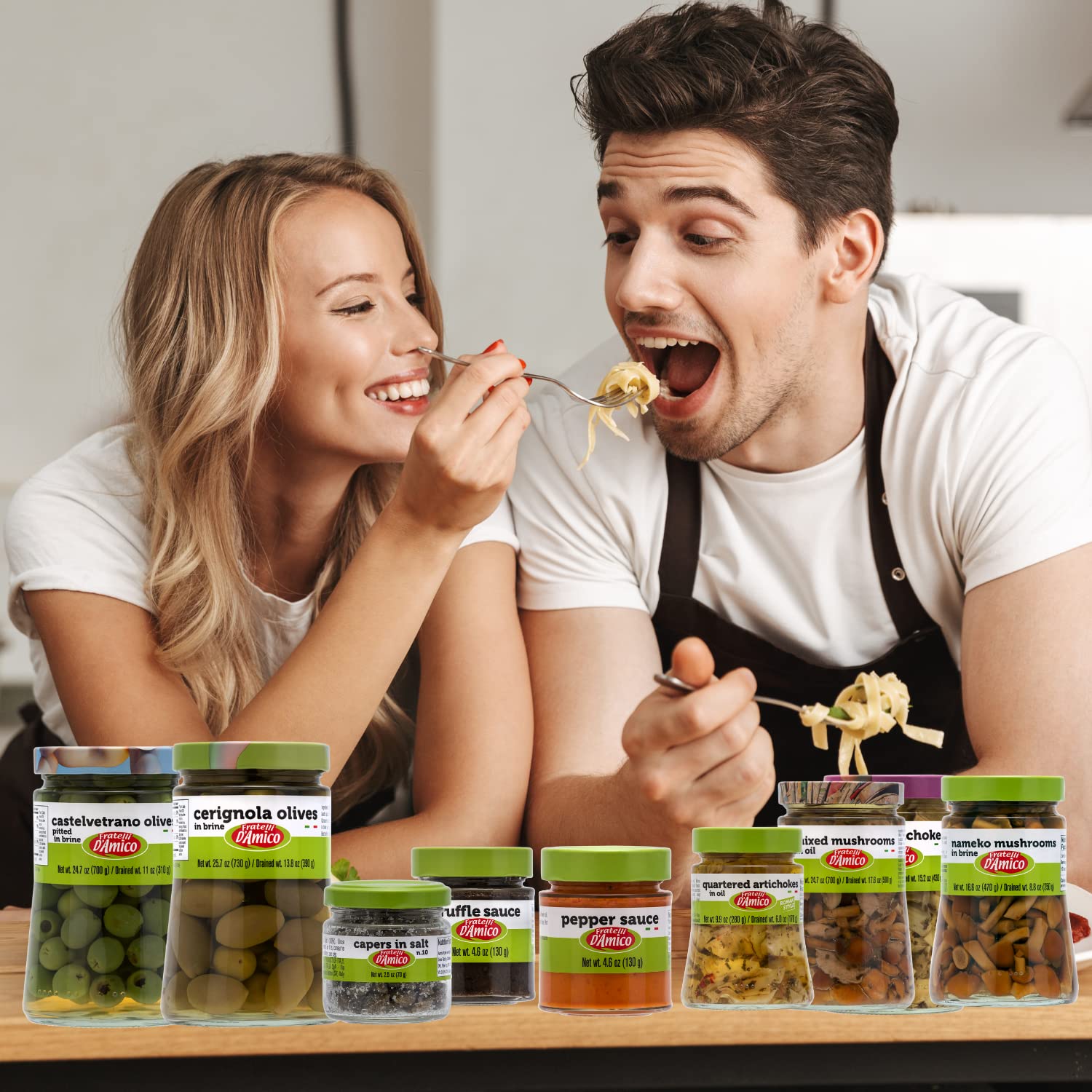 Smiling couple enjoying pasta together with a selection of Fratelli D’Amico Italian gourmet products including olives, truffle sauce, pepper sauce, capers, artichokes, and mushrooms displayed on the table.