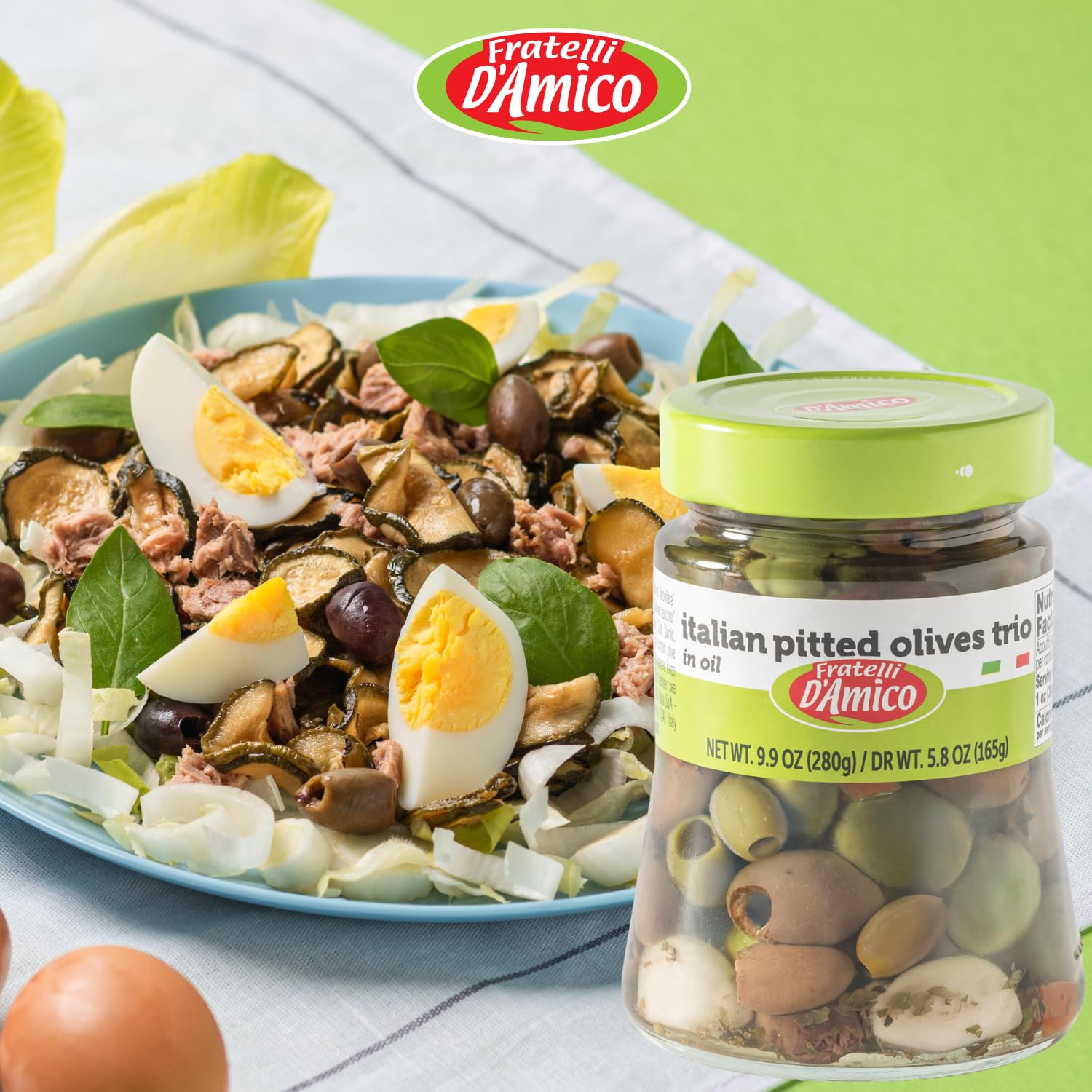 Fratelli D’Amico Italian Pitted Olives Trio jar displayed in front of a fresh Mediterranean salad with boiled eggs, tuna, and zucchini, perfect for authentic Italian cuisine.