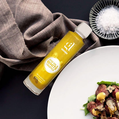Bottle of GL Truffle Extra Virgin Olive Oil with White Truffle placed beside a gourmet dish and sea salt on a dark background.