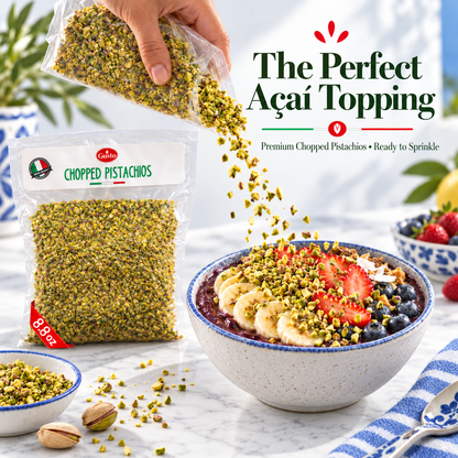 A hand pours chopped pistachio topping from a clear bag into a bowl of smoothie topped with sliced banana, strawberries, blueberries, and more pistachios. A branded bag of chopped pistachios, a small bowl, and the text 'The Perfect Açaí Topping' are visible on a bright kitchen-style background.