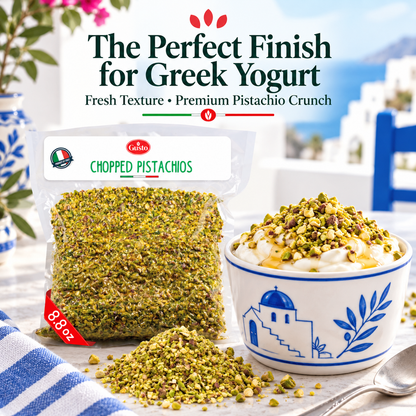 A bag of Gusto Etna Chopped Pistachios shown next to a bowl of Greek yogurt topped with chopped pistachios, with a pile of loose pistachios in front. The background features a blurred Mediterranean scene with white buildings and blue water.
