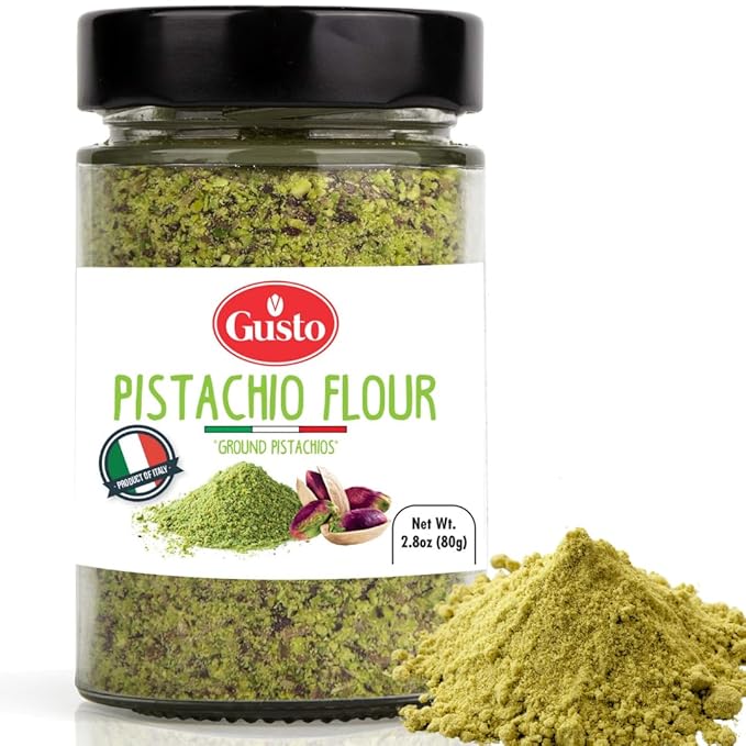 A jar of Gusto Pistachio Flour with a black lid and a white label, shown alongside a pile of green pistachio powder on a white background.
