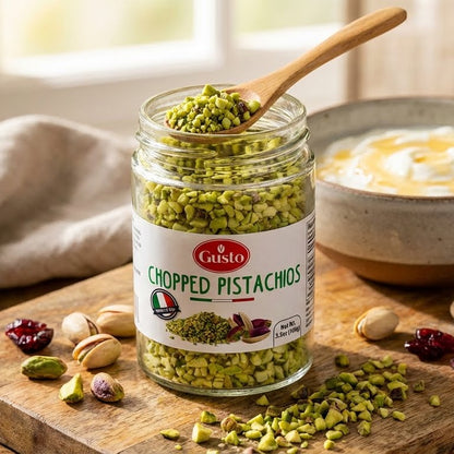 Jar of Gusto chopped pistachios with a wooden spoon on a wooden surface.