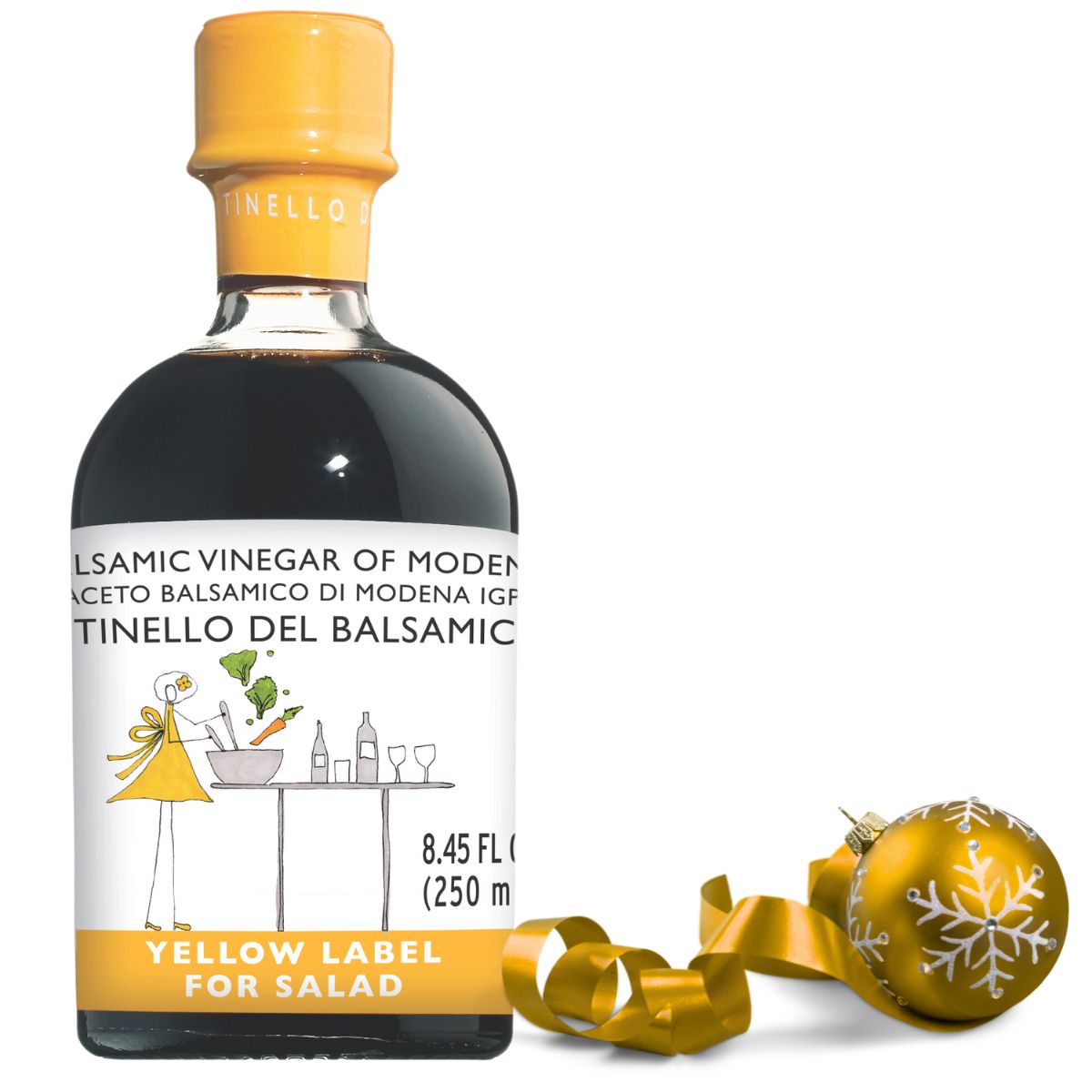Bottle of Tinello Del Balsamic vinegar with a yellow label and decorative ball on a white background