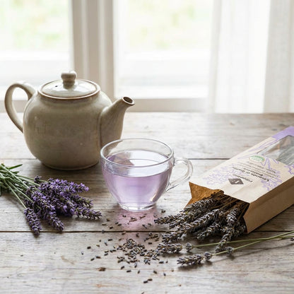 Tea set with a teapot, glass of lavender tea, and lavender flowers on a wooden table.