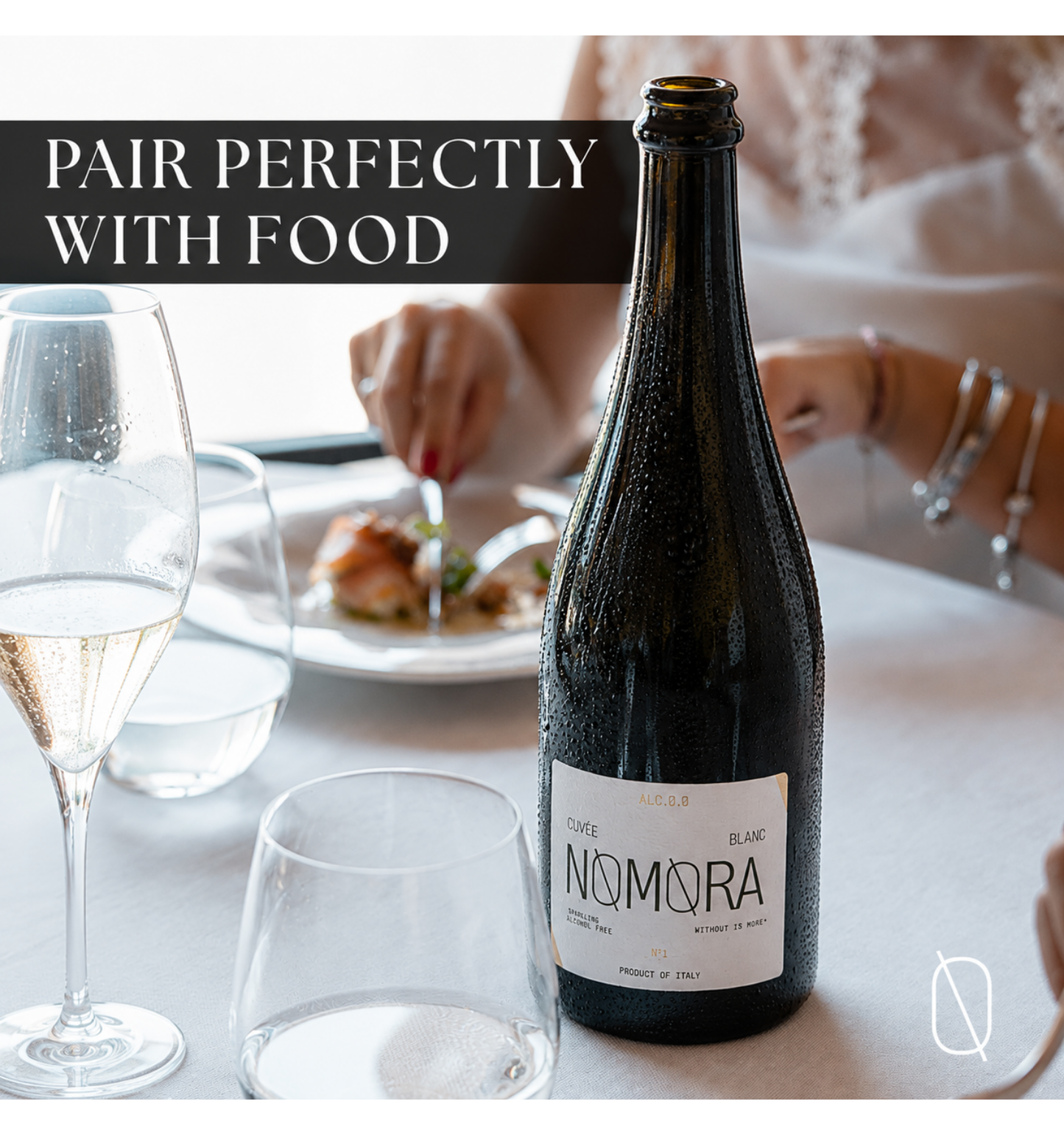 A bottle of Nomora sparkling wine stands on a table in a dining setting, with a wine glass, water glass, plates, and hands in the background. Text at the top reads 'PAIR PERFECTLY WITH FOOD'.
