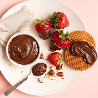 Strawberries dipped in hazelnut dark cocoa spread, served with wafers, hazelnuts, and a bowl of creamy chocolate spread on a white plate.