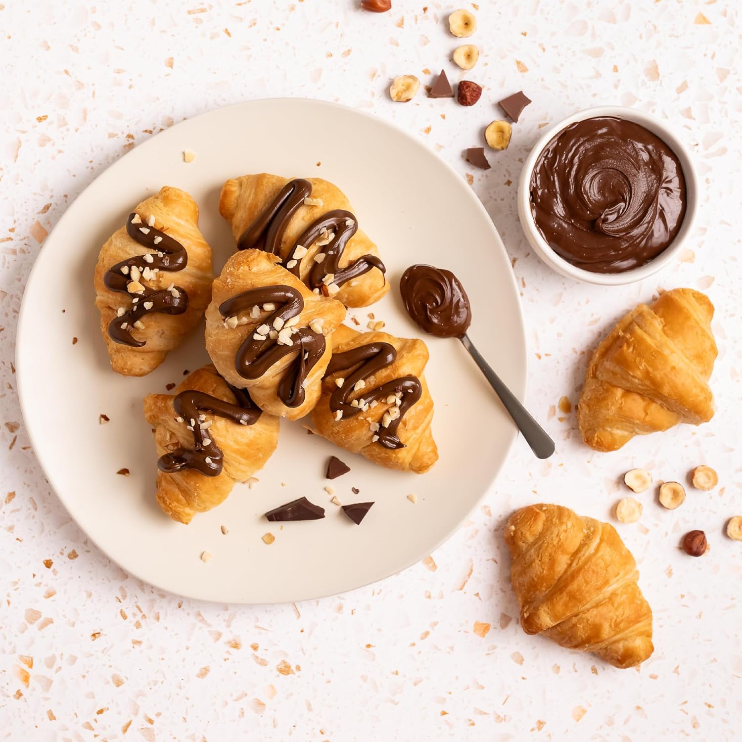 Croissants topped with Nutlicious hazelnut espresso spread and chopped hazelnuts on a white plate.