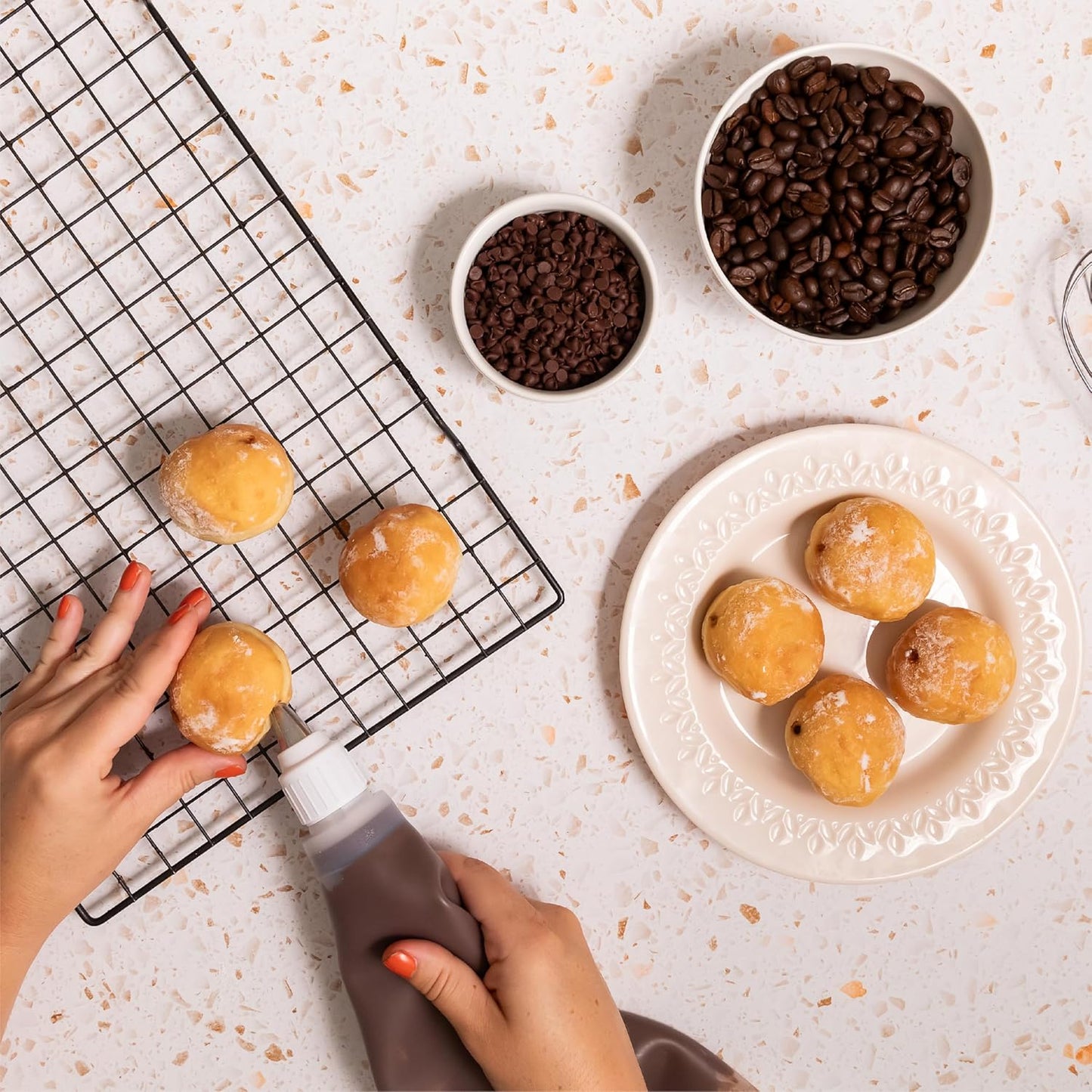 Mini donuts being filled with Nutlicious Hazelnut Mocha Spread using a piping bag, surrounded by bowls of chocolate chips and coffee beans on a light surface