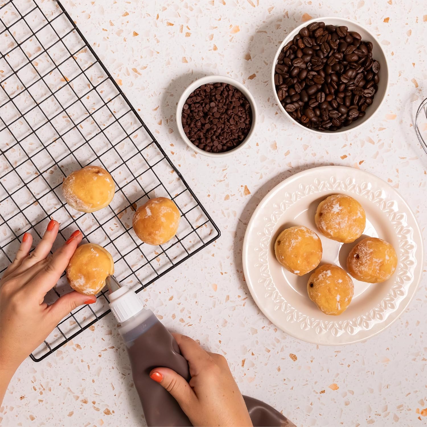 Mini donuts being filled with Nutlicious Hazelnut Mocha Spread using a piping bag, surrounded by bowls of chocolate chips and coffee beans on a light surface
