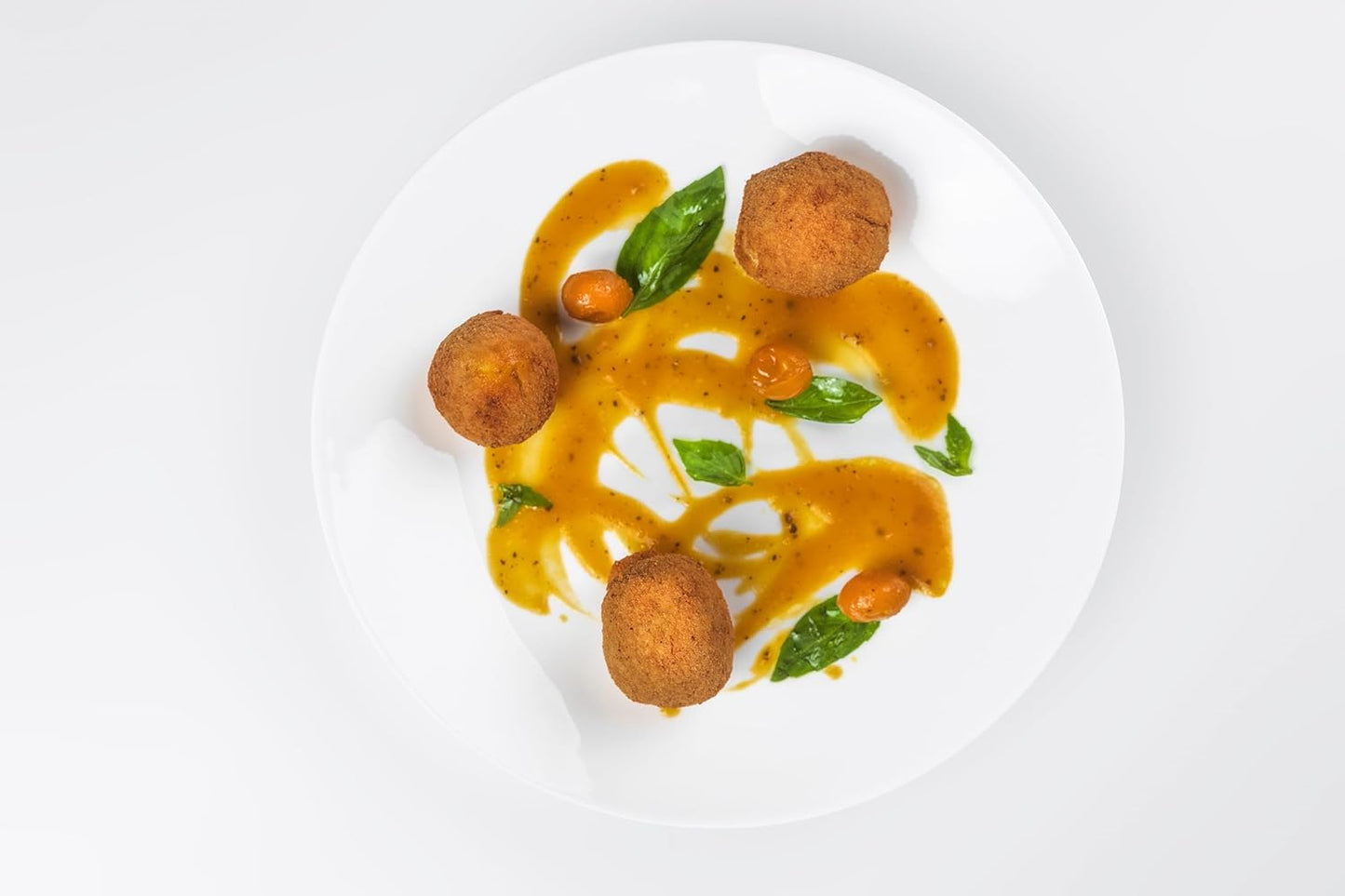Plated dish with fried balls and a yellow sauce on a white background