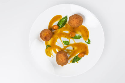 Plated dish with fried balls and a yellow sauce on a white background