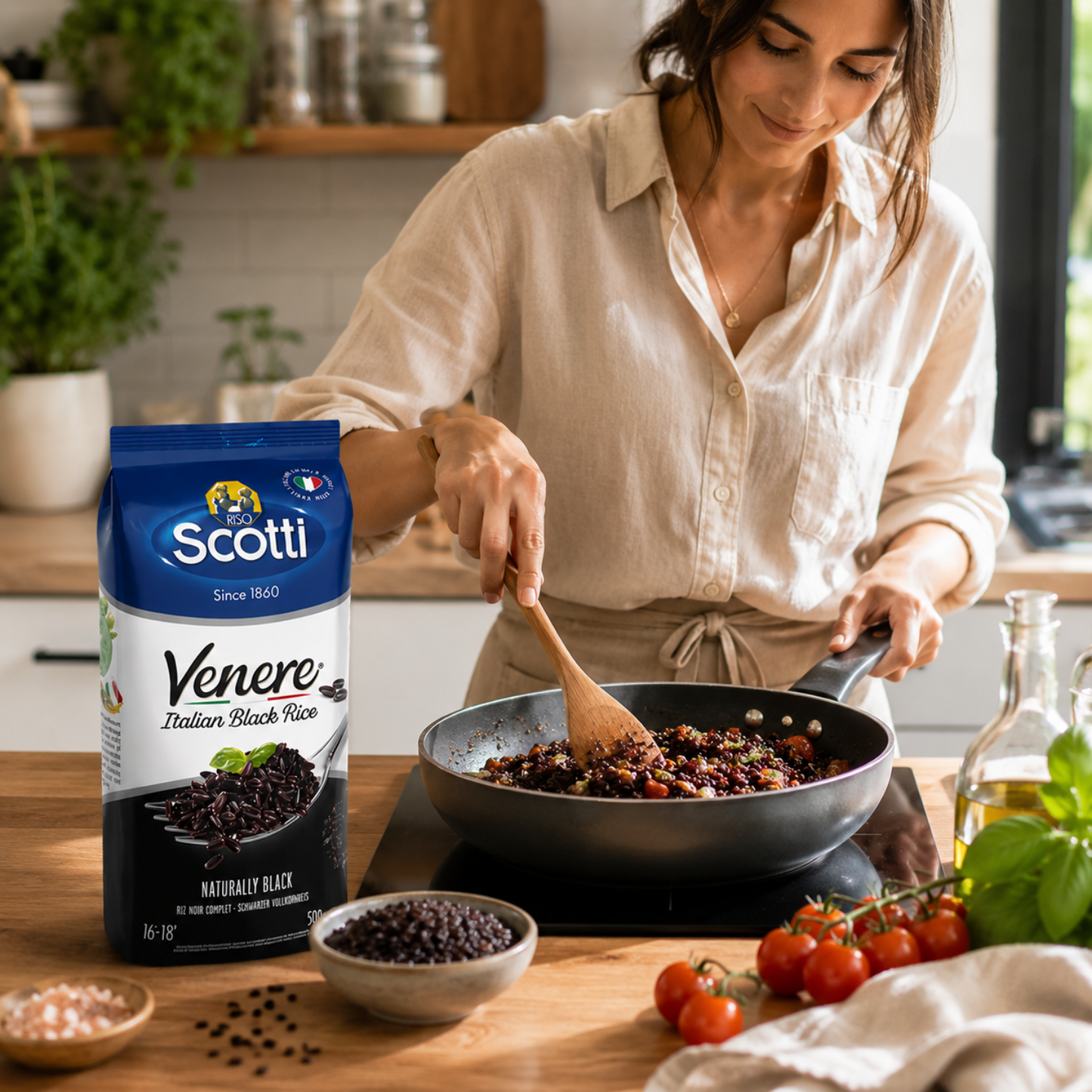 A woman in a cream shirt stirs a pan of food in a kitchen, with a bag of Scotti Venere Italian Black Rice placed on the counter beside her.