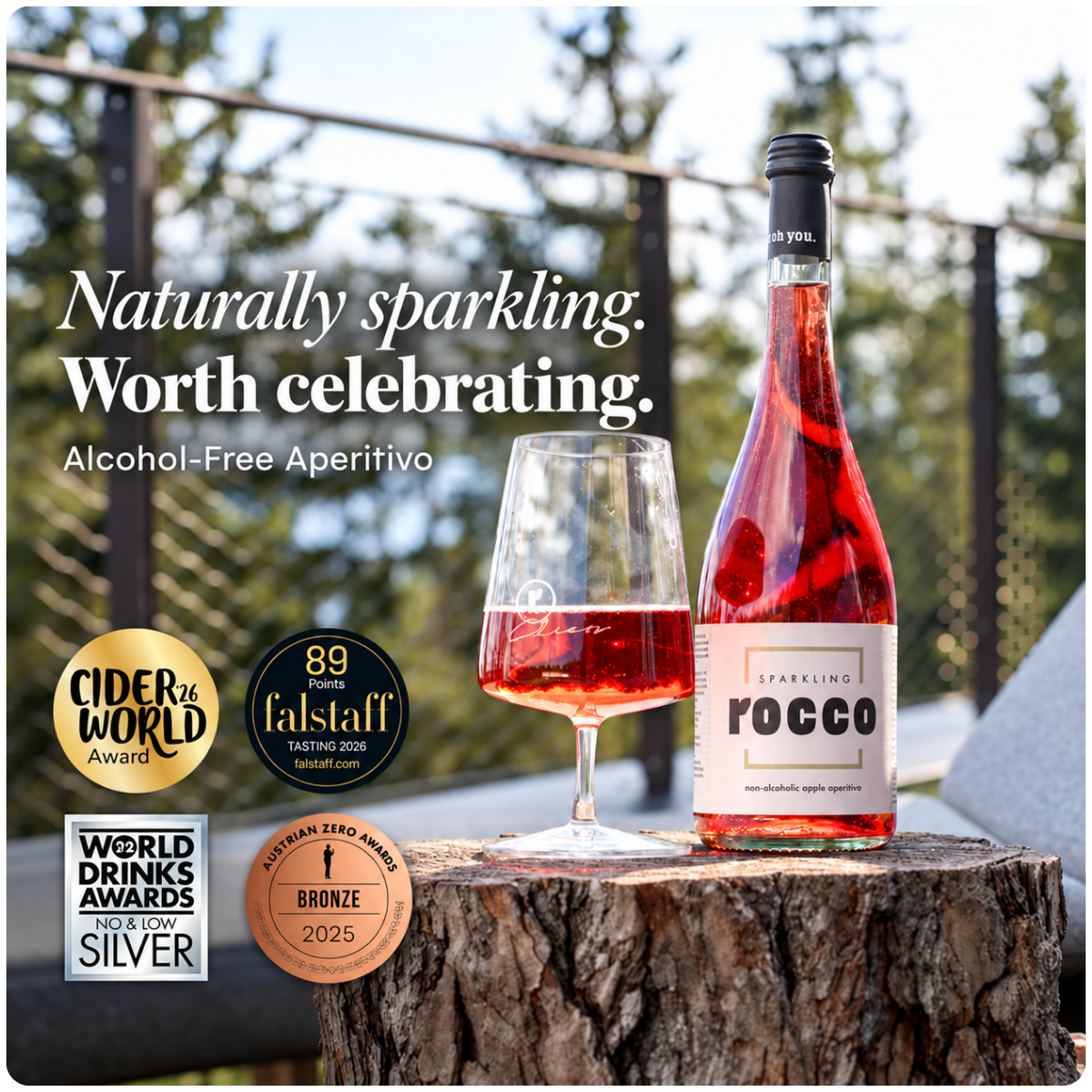 A bottle of Rocco Alcohol-Free Sparkling Aperitivo and a filled wine glass sit on a tree stump outdoors, with promotional text and award badges on the left side of the image.