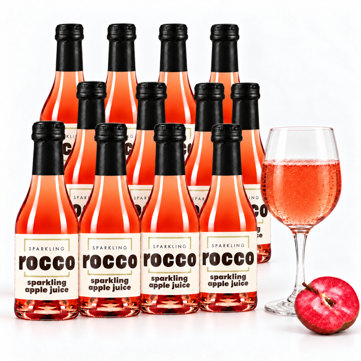 A set of Rocco Sparkling Apple Juice bottles arranged in rows, with a glass of the pinkish-orange sparkling drink and a red apple on a clean white background.