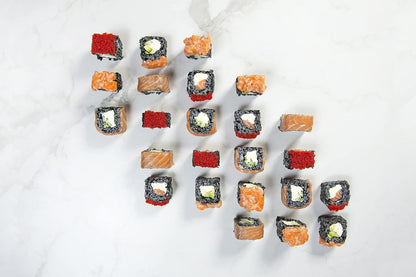 Assorted sushi rolls arranged neatly on a white marble surface. The rolls are made with black rice and filled with ingredients such as salmon, cucumber, avocado, and cream cheese, some topped with bright red fish roe.