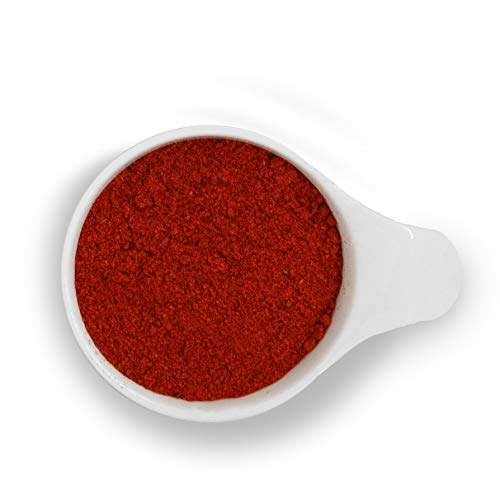 White measuring spoon filled with red powder on a white background