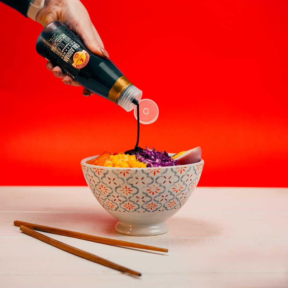 Person pouring soy sauce into a bowl of salad with a red background