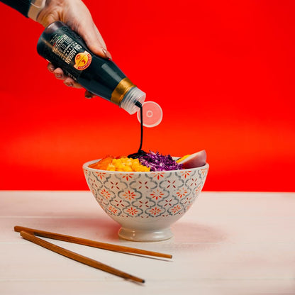 Person pouring soy sauce into a bowl of salad with a red background
